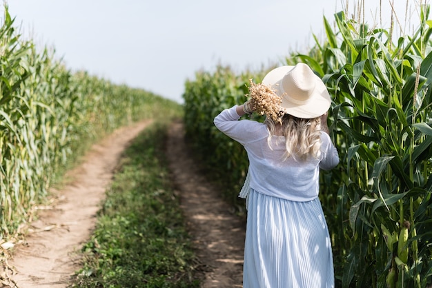 A girl in a straw hat walks in the corn field