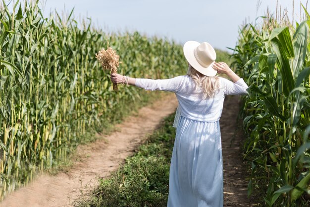 A girl in a straw hat walks in the corn field