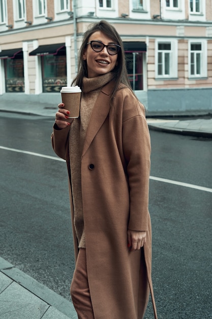 Ragazza per strada con un bicchiere di carta usa e getta. porta via il cibo, cammina per la città.