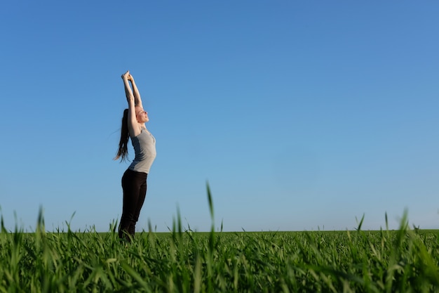 Girl stretching herself in green field with blue sky