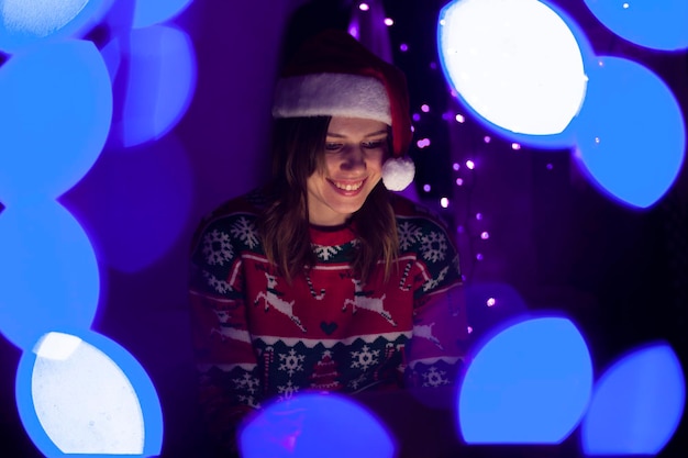 Girl student in Christmas clothes sits at home with a laptop at night