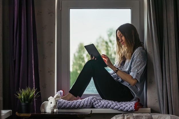 Girl student communicates and studies at home near the window\
on the tablet