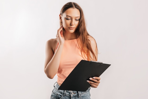 Girl student frowns with displeasure and reads information in documents. Beautiful young business woman holds a clipboard with mockup on gray background. Study and business concept. Online learning