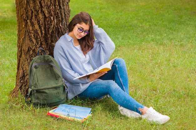 A girl, a student in glasses reads a book in nature.