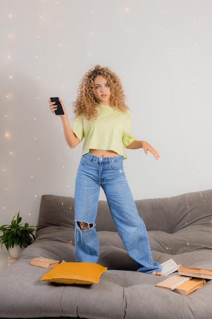 Girl student has taken break from preparing for exams and is dancing and having fun among the books scattered on the gray sofa. concept of education and recreation. space for text. High quality photo