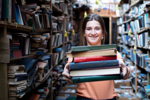 Girl student holds a stack of books in the library, she searches for literature and offers to read, a woman prepares for study, knowledge is power, concept bookseller
