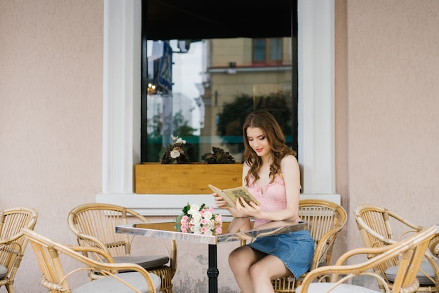 Фото Девушка-студентка романтически читает книгу за столом в уличном кафе
