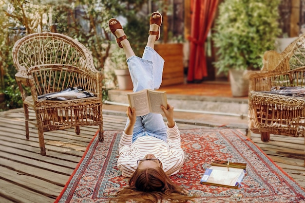 girl student reading a book lying on the floor on a carpet in vintage style