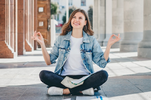 Girl student sitting on the floor and meditating. lovely girl asks for a good grade in the exam. girl prays in lotus position.