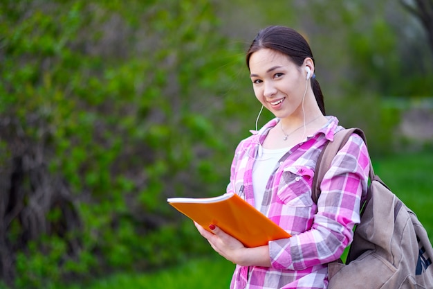 Girl student smiling and holding a stack of folders in summer park