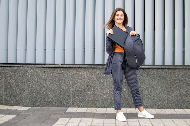 Girl student stands against a wall and takes a laptop from a backpack