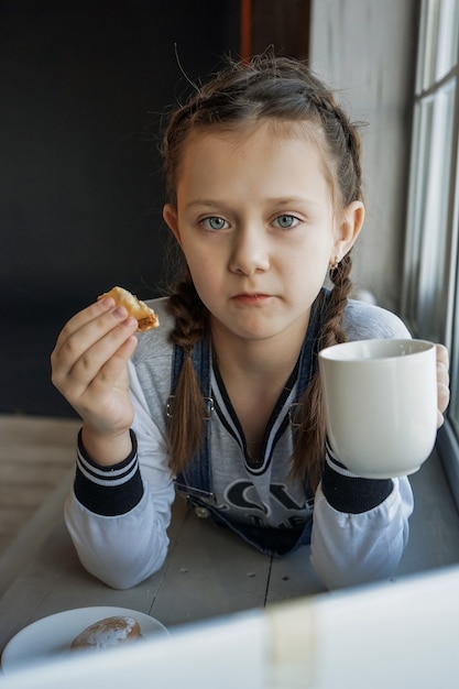 La studentessa studia online con l'insegnante di videochiamata, la ragazza felice ascolta la lezione guarda al computer portatile a casa e beve il tè e? mangiare i biscotti. covid-19-coronavirus.