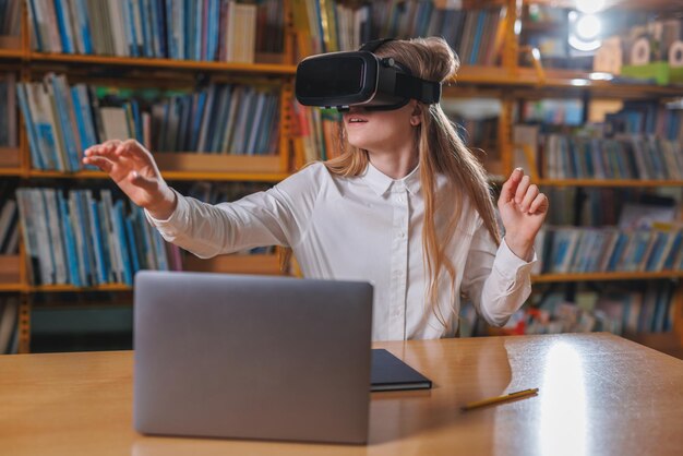 Girl student using modern tech devices in the library a laptop and VR headset Concepts of virtual reality experience in education