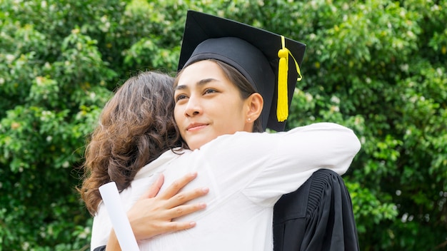 卒業式のガウンと帽子を持つ女子学生は、お祝い式で親を抱擁します。