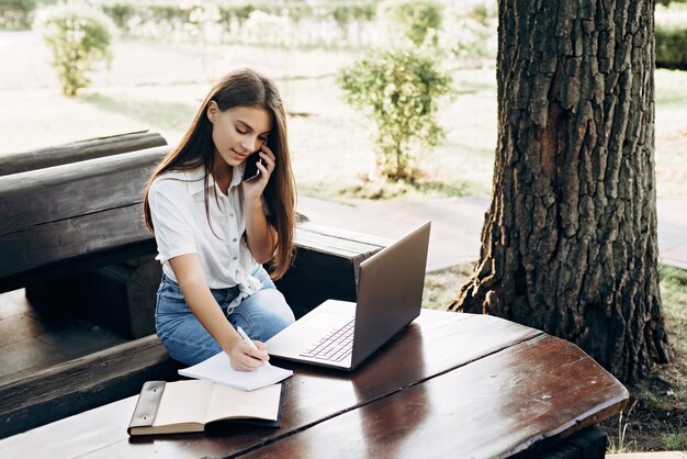 Girl student with a laptop outdoors sits on the grass in the park