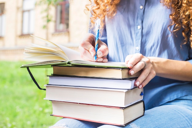 Girl student with long curly hair writes in a notebook on a pile of books