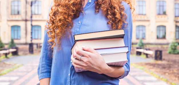 Studentessa con lunghi capelli rossi ricci con una pila di libri di testo dalla biblioteca