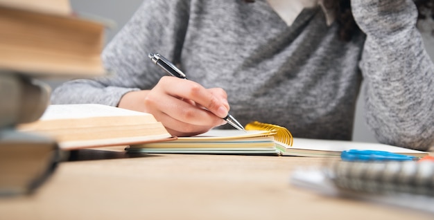 Girl student writing in notebook with stack books