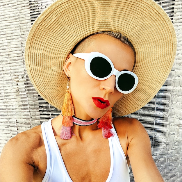 Girl in stylish beach accessories. Sunglasses, earrings, hat. Beach fashion outfit.