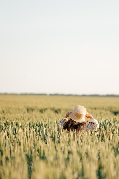 A girl in a stylish dress walking on a field of ripe wheat in the rays of the setting sun Wheat ear Rye ears Selective focus Setting sun Walk in the rye field