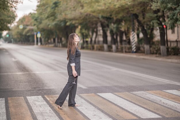 A girl in a suit crosses a pedestrian crossing with a glass of wine in the summer