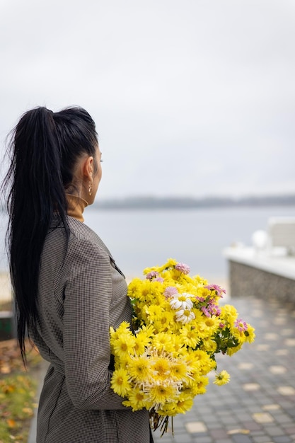 a girl in a suit stands with yellow flowers by the river