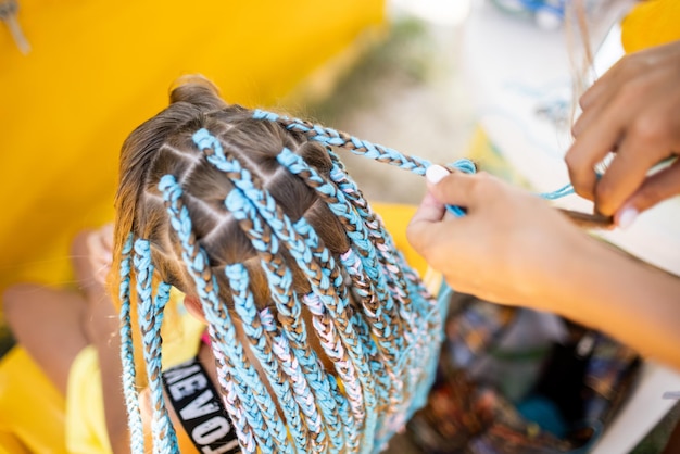 A girl in a suit weaves African braids in her hair on a sunny day