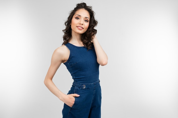Girl in summer blue overalls posing on a gray background with copy space