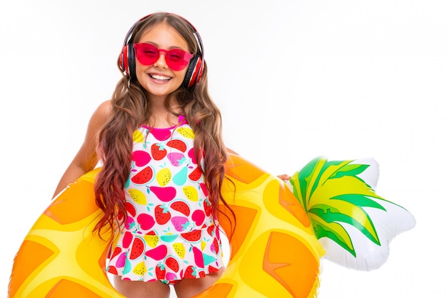 Girl in sunglasses and a baseball cap listens to music on headphones with a lifeline bright swimming circle on a white wall