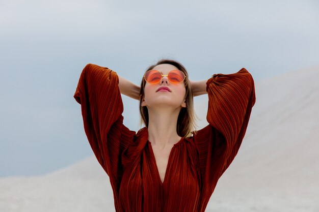 Girl in a sunglasses and burgundy color blouse on a white sand