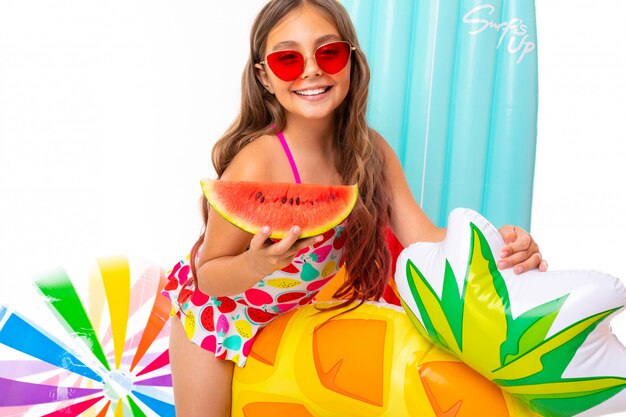 Girl in sunglasses with a piece of watermelon on the wall of air mattresses, balls and circles