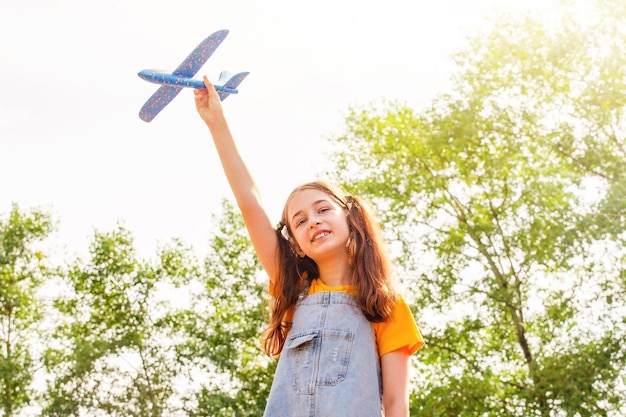 화창한 날의 소녀 하늘과 나무를 배경으로 파란 장난감 비행기를 손에 들고 있는 10대 소녀