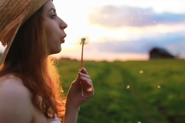 Girl at sunset field blow dandelion