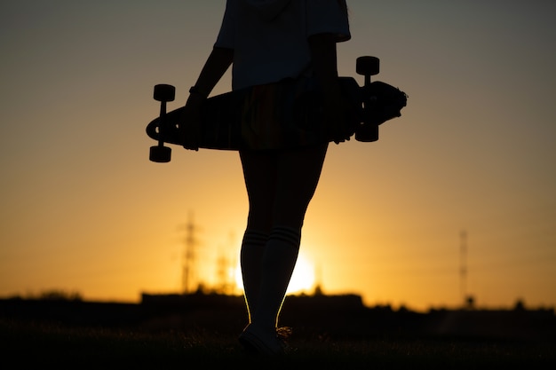 Ragazza al tramonto con un longboard in mano