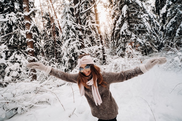 A girl in a sweater and glasses walks in the snow-covered forest in winter