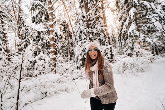 A girl in a sweater and glasses walks in the snow-covered forest in winter