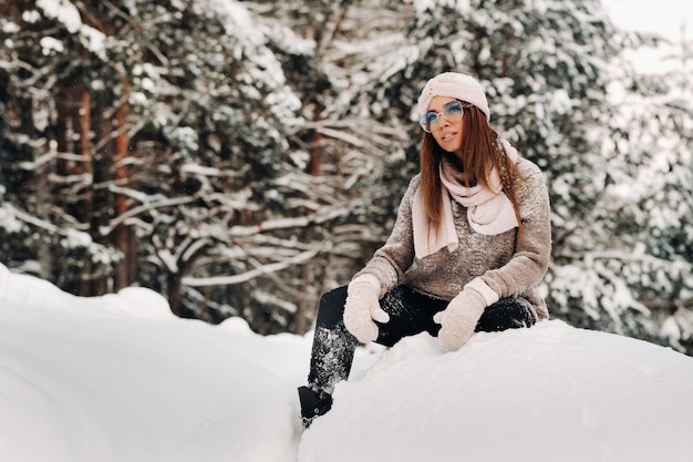 A girl in a sweater and glasses in winter sits on a snow-covered