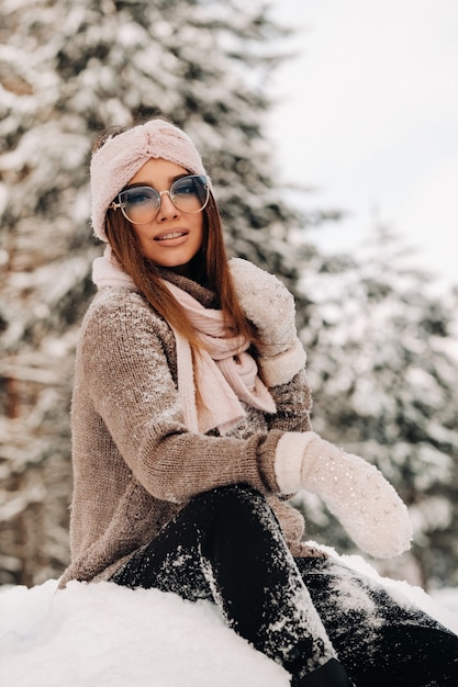 A girl in a sweater and glasses in winter sits on a snow-covered