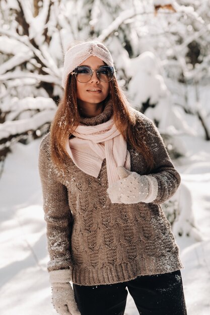 A girl in a sweater and glasses in winter in a snow-covered forest