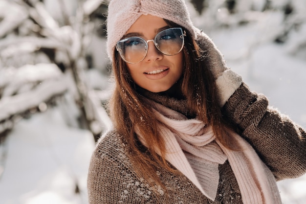 A girl in a sweater and glasses in winter in a snow-covered forest