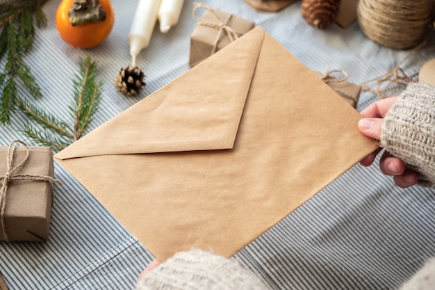 A girl in a sweater holds a craft envelope on a new year's surface. The concept of a letter to Santa, wish list.