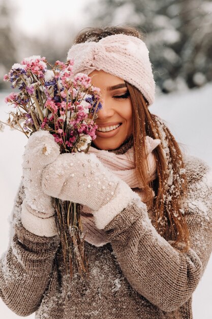 大きな雪の吹きだまりの中に、花束を手にした冬のセーターを着た女の子が立っています。