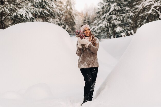 A girl in a sweater in winter with a bouquet in her hands stands among large snowdrifts.