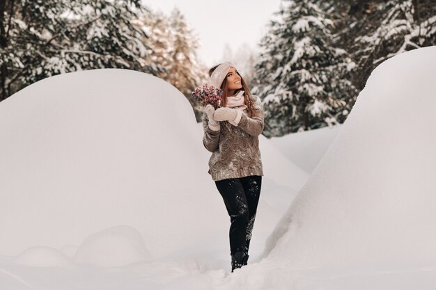 Девушка в свитере зимой с букетом в руках стоит среди больших сугробов.