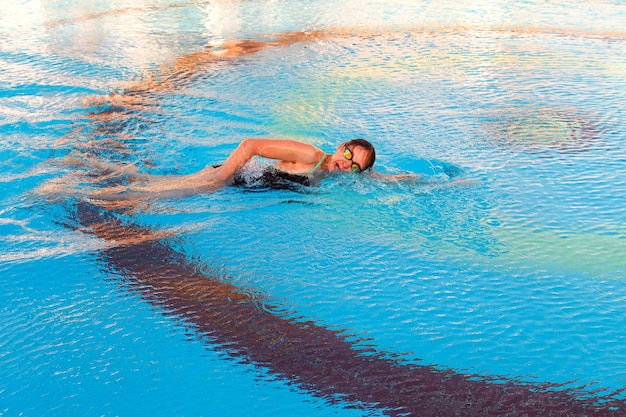 The girl swims in the pool in crawl style