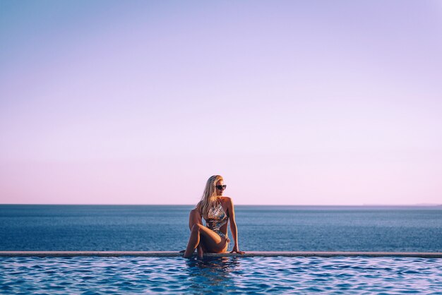 La ragazza in costume da bagno vicino alla piscina panoramica sullo sfondo del mare si rilassa