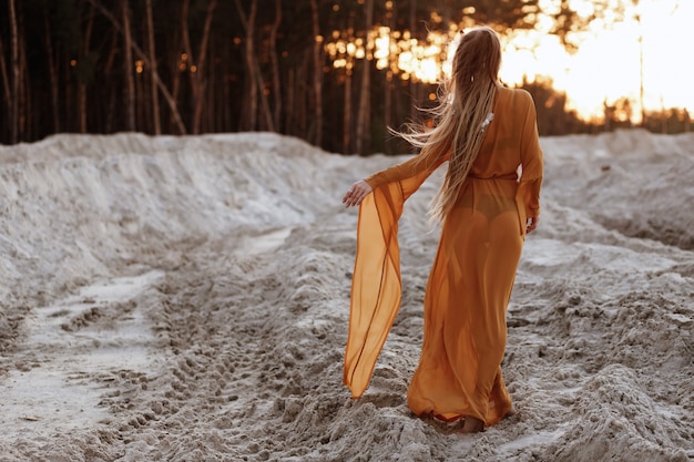 일몰 모래에 수영복과 투명 갈색 드레스 소녀