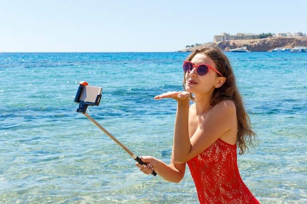 Girl in swimsuit with a smart phone on the beach. Girl taking fun selfie at the beach