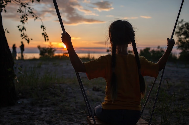 秋の夕日の家族の散歩の海でスイングの女の子秋の雰囲気旅行アクティブなライフスタイル