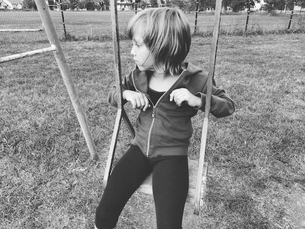 Girl on a swing Monochrome retro photography A child in a sports uniform is swinging In the background is the stadium Sadness on the face The emotion of frustration and the feeling of loneliness